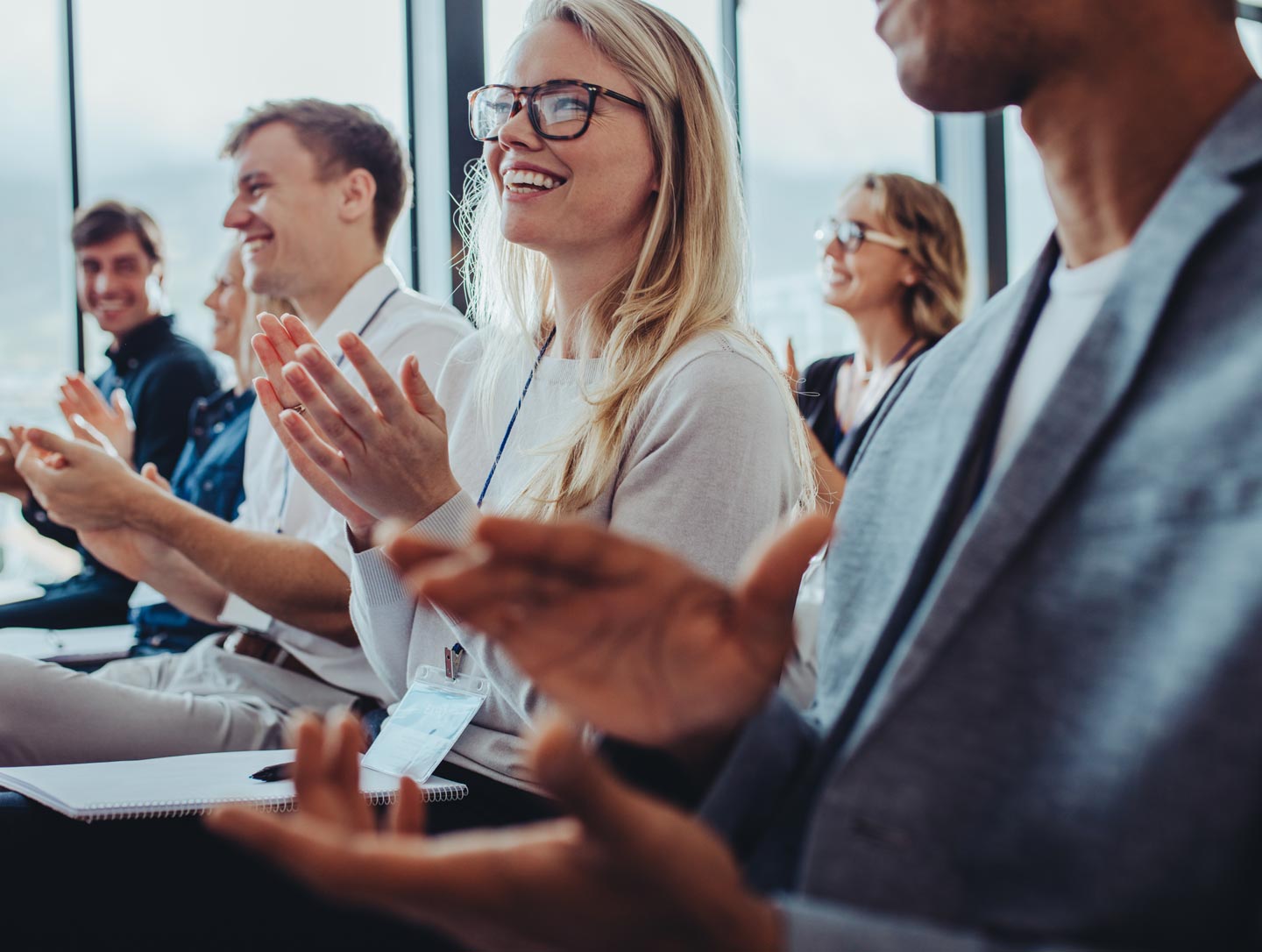 Close up of a seated crowd of professional audience members smiling and applauding during a technical seminar presentation.
