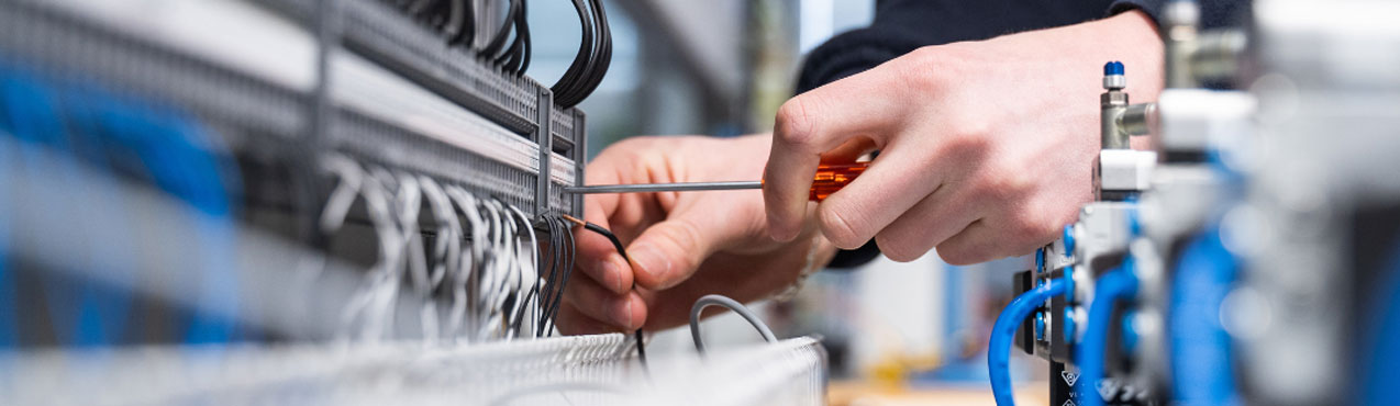 Close up view of a technician's hands using a screwdriver to precisely integrate electrical wiring and terminal connections on an industrial panel.